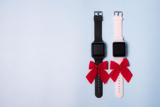 The watch is white and black electronic with a bow on a plain background . The watch is handmade with a bow . Gift watch is white with a red bow on a blue background. Modern watches. Pedometer. A gift for the holiday. Blue background. Watch as a gift