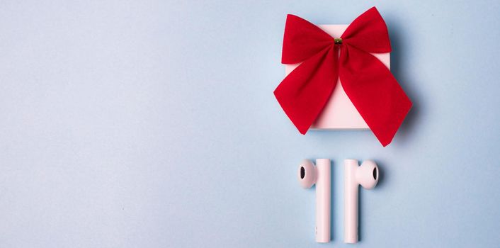 Gift wireless headphones . White wireless headphones. Modern gadgets. Headphones for music. The layout of the top view. Copy space . red bow. Blue background