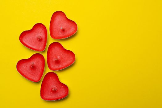 Candles in the form of hearts on a yellow background . Red candles. Red hearts. Yellow background. Copy space. Valentine's Day. Holiday. An article about celebrating Valentine's Day.. An article about love.