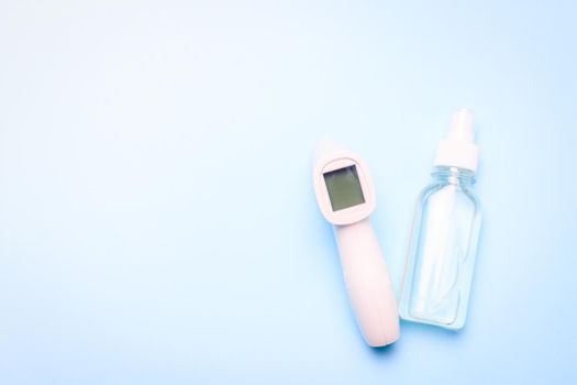 infrared thermometer and antiseptic on a blue background . antiseptic. treatment of hands. prevention. non-contact temperature measurement. health. coronavirus. pandemic. human health. check the temperature. copy space