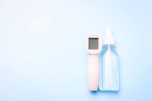 infrared thermometer and antiseptic on a blue background . antiseptic. treatment of hands. prevention. non-contact temperature measurement. health. coronavirus. pandemic. human health. check the temperature. copy space