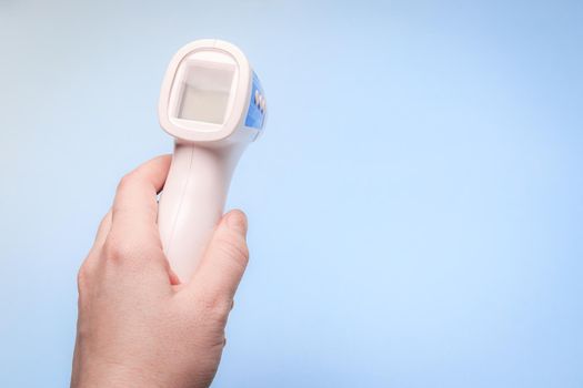 infrared thermometer on a blue background in your hand. the thermometer in his hand . prevention. non-contact temperature measurement. health. coronavirus. pandemic. human health. check the temperature. copy space