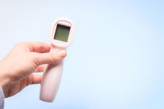 infrared thermometer on a blue background in your hand. the thermometer in his hand . prevention. non-contact temperature measurement. health. coronavirus. pandemic. human health. check the temperature. copy space