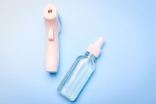 infrared thermometer and antiseptic on a blue background . antiseptic. treatment of hands. prevention. non-contact temperature measurement. health. coronavirus. pandemic. human health. check the temperature. copy space