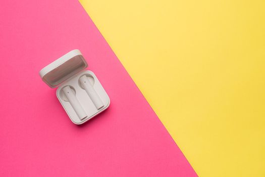 Wireless headphones on a pink background . Bright background. White headphones. Bluetooth headset. Pink and yellow background. Copy space. An article about technology. Modern technologies.