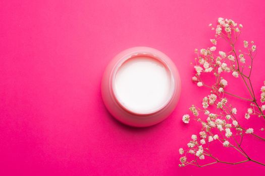 Cream for face in flowers . Face cream on a pink background. Skin care. The beauty industry. Copy space. White flowers. Article about the right choice of cream. Selection of the cream. Spa treatments. Cosmetology.