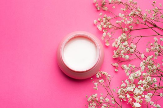 Cream for face in flowers . Face cream on a pink background. Skin care. The beauty industry. Copy space. White flowers. Article about the right choice of cream. Selection of the cream. Spa treatments. Cosmetology.