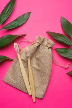 Bamboo toothbrushes and a canvas bag on a pink background. Green leaves. Eco products. No plastic. Health and medicine. Dentistry. Brushing your teeth. Copy space. An article about taking care of the environment.