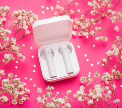 Wireless headphones and white flowers . Modern technologies. Headphones in the case. Listen to bluetooth music. Flowers. White flowers. Pink background