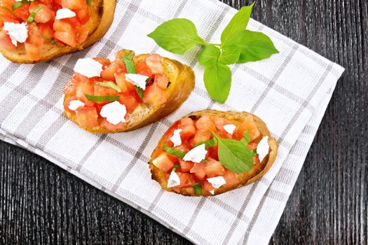 Bruschetta with tomato, basil and soft cheese on a napkin on dark wooden board from above