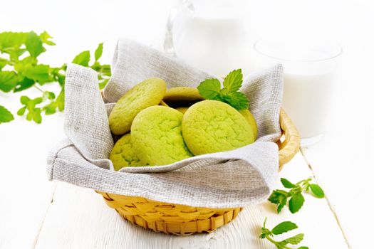 Green mint cookies on napkin in wicker basket, milk in a glass and a jug on wooden board background