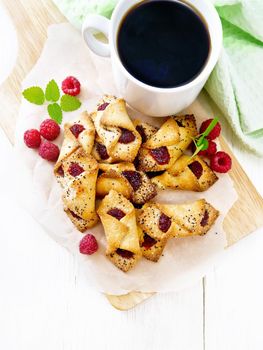 Cookies with raspberry jam, berries and mint on parchment on a plank, cup with coffee and napkin on wooden board background from above