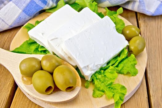 White brine cheese, lettuce, olives, spoon with olives, blue plaid napkin on a wooden boards background