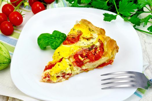 Piece of cake of zucchini with tomatoes and eggs, basil in a plate on a napkin, parsley on a wooden boards background