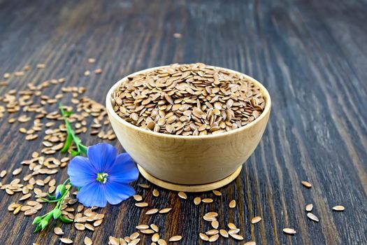 Seeds of linen brown in a bowl, blue flax flower on a wooden plank background