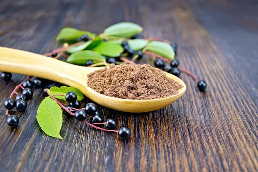 Flour of bird-cherry in a spoon with berries and green leaves on a background of wooden boards