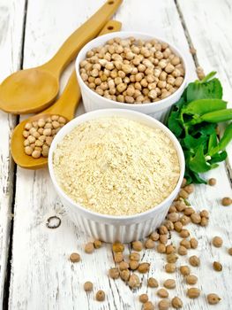 Flour chickpeas and chick-pea in white bowls and spoons, pods of green beans on the background of wooden boards