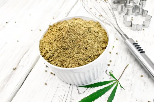 Hemp flour in a bowl, mixer and cookie cutters, cannabis leaves on the background light wooden boards