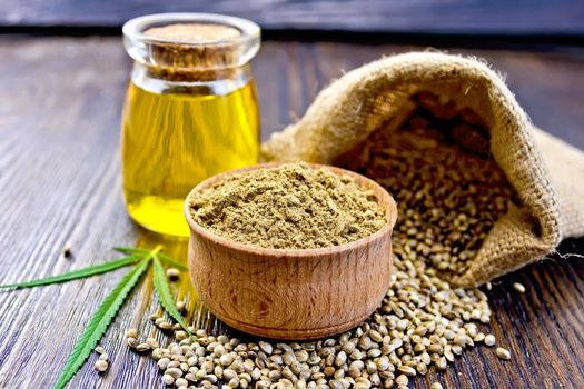 Hemp Flour in a wooden bowl, hemp seed in a bag and on the table, hemp oil in a glass jar, hemp leaf on the background of wooden boards