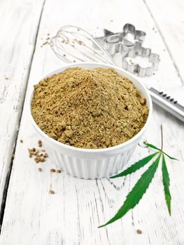 Hemp flour in a bowl, mixer and cookie cutters, cannabis leaves on the background wooden boards