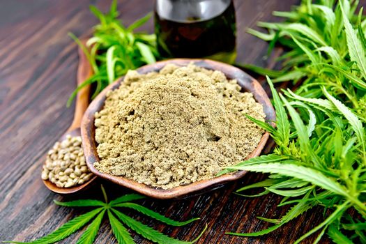 Hemp flour in a clay bowl, grain in a spoon in a glass jar oil, cannabis leaves on the background of wooden boards