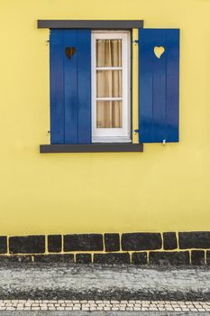 Blue window with hearts, yellow wall and street.