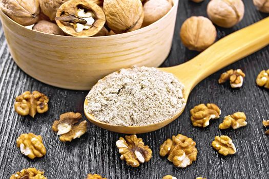 Walnut flour in a spoon, nuts in bowl and on table on background of wooden board