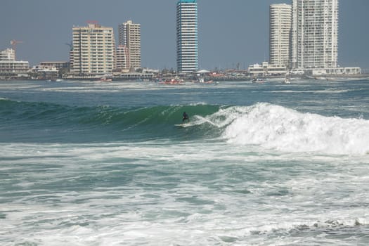 Man surfing on a wave in Iquique Chile with view of city in background.