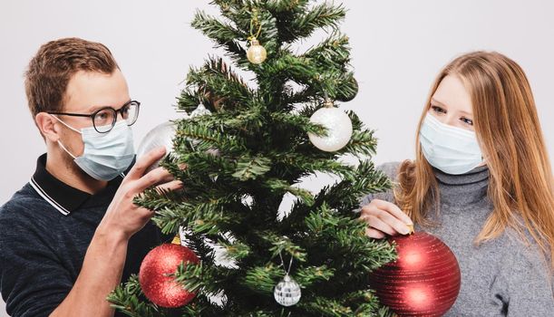 Couple decorating the Christmas tree with ornaments wearing covid-19 face mask
