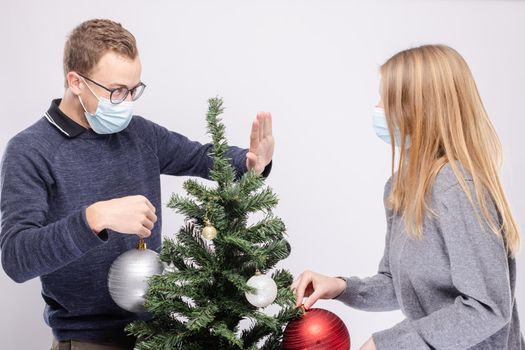 Couple trying to maintain social distancing while decorating Christmas tree wearing mask