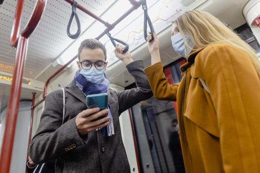 People using phone in train wearing covid-19 face mask during their commute