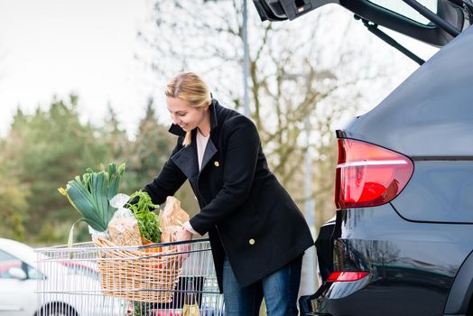 Woman loading groceries after shopping into trunk of her car on parking spot