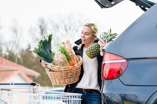 Woman loading groceries after shopping into trunk of her car on parking spot