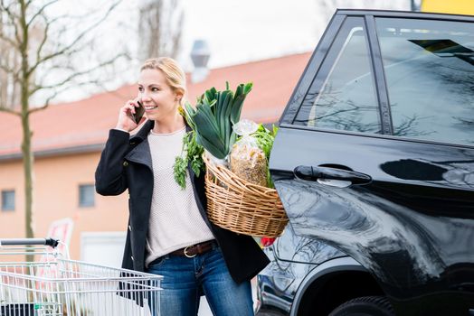 Woman using phone while storing groceries in trunk of her car