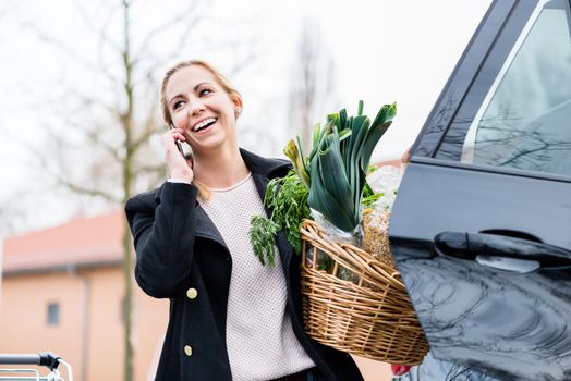 Woman using phone while storing groceries in trunk of her car