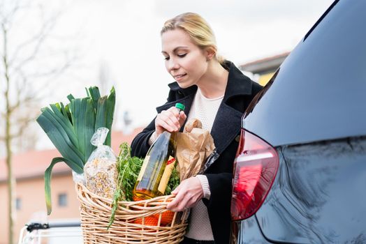 Woman storing basket with groceries into trunk of car after shopping