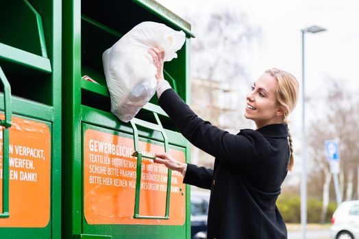 Young woman putting old or used clothes into donation bin