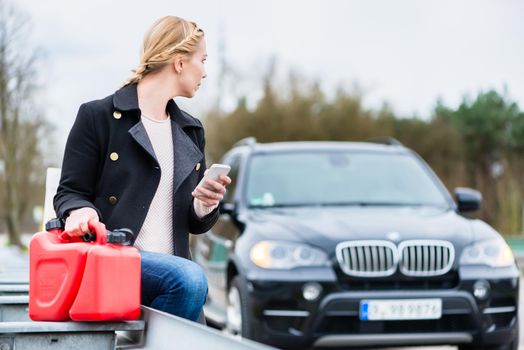 Woman has car with empty gas tank calling for help on phone holding spare canister in hand