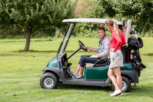 Fit young woman talking to male golfer sitting in the golf cart