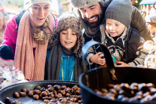 Family with two kids on Christmas market eating sweet roasted chestnuts