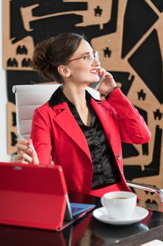 Businesswoman in her office sitting at the desk with phone and coffee