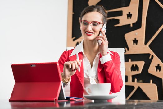 Businesswoman in her office sitting at the desk with phone and coffee