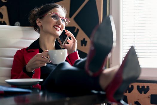 Businesswoman having a coffee using the phone putting feed on desk in relaxed pose