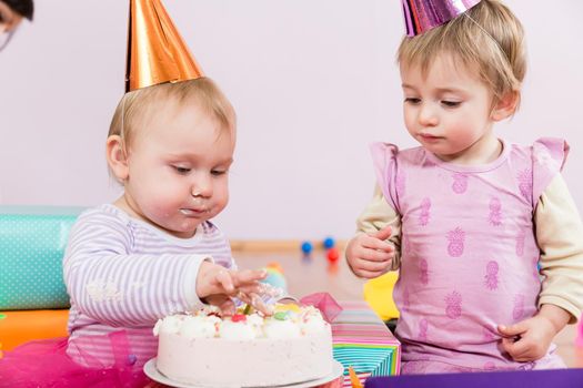 Two toddlers with party heads with birthday cake