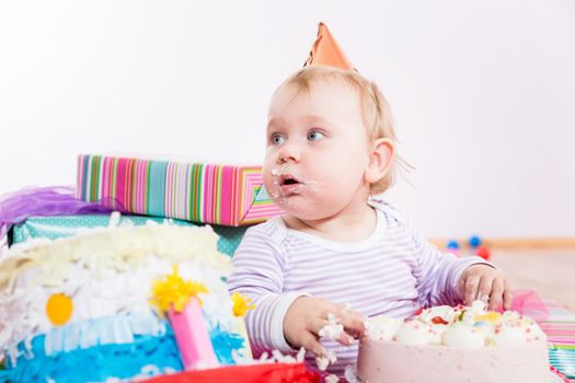 Toddler in the middle of many presents eating birthday cake