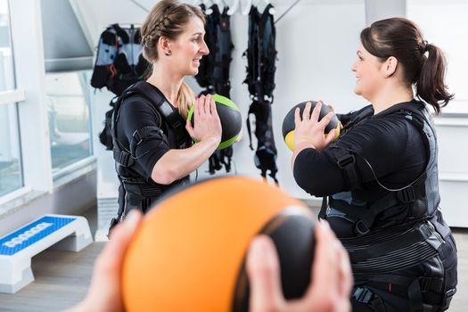Skinny and big woman having fun during ems training with medicine ball