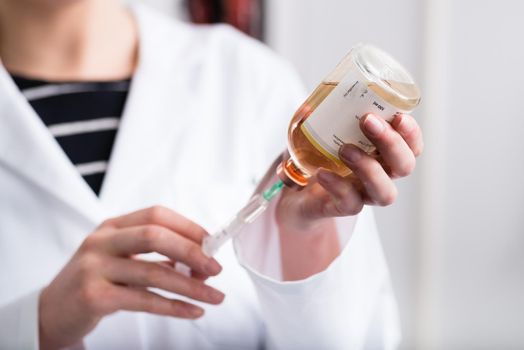 Close-up of a doctor's hand holding syringe and a injection solution bottle