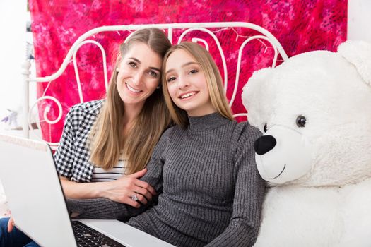 Mother and daughter having fun with the computer in a bedroom