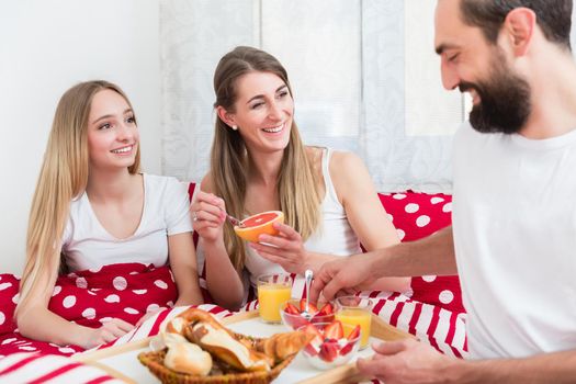 Family of three having its breakfast together in bed