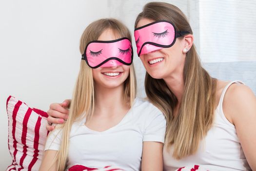 Mother and daughter wearing pink sleeping masks in bed